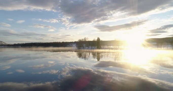 4K wide drone shot with parallax motion of beautiful calm lake with mist fog in golden hour with reflections of vibrant sunset and cloudy blue sky in winter, in Oslo Norway.