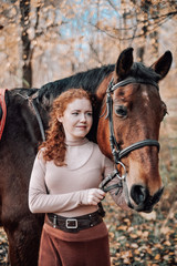 Fototapeta premium Portrait of beautiful red haired woman with horse outdoors.