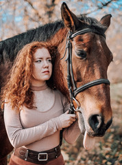 Fototapeta premium Portrait of beautiful red haired woman with horse outdoors.