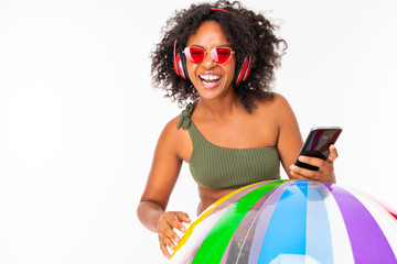 Pretty african female in swimsuit stands with big colourful rubber ball, listen to music with...