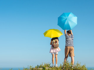 Back of boy and girl holding yellow and blue umbrella with top of city view background.