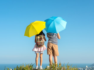 Back of boy and girl holding yellow and blue umbrella with top of city view background.