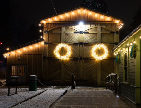 Barn house decorated with christmas lights photographed on a winter night, this wreath stands out against the weathered wooden background.