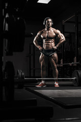 Muscular athletic bodybuilder fitness model training and posing with barbell in gym. Concept sport...