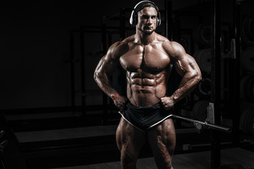 Muscular athletic bodybuilder fitness model training and posing with barbell in gym. Concept sport...
