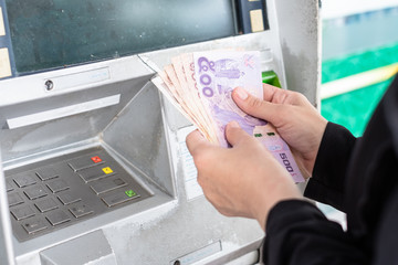 Close up of hand withdraw money in Thai baht currency from bank machine.  Cash out money at an ATM.