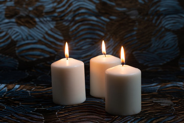 Three lit white candles on dark background.