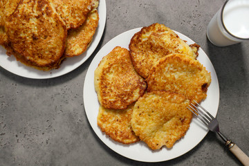 2 plates with potato pancakes on a gray background, a glass of milk, a fork,