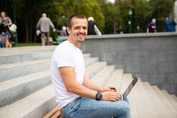 Fototapeta premium Man freelancer with laptop sitting in urban park