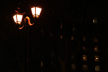 Night illumination of winter park in the central part of the town. Old-fashioned city lantern, covered with snow on the black background. Merry Christmas and Happy New Year