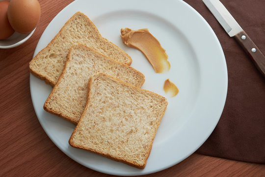 Whole wheat breads and peanut cream,knift,napkin in white plate on white on wooden table.