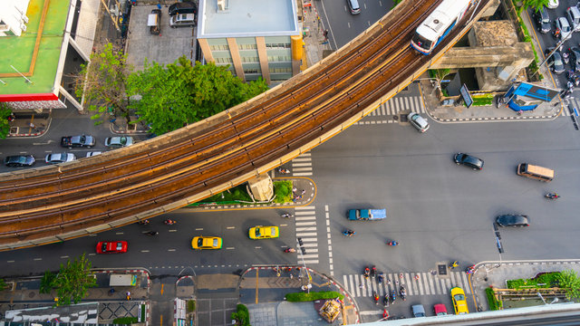 Top view aerial of a driving car on asphalt track and pedestrian crosswalk in traffic road  with sky train run on the top rail.