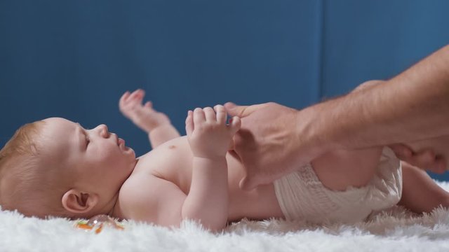 Dad changes diaper pants baby. A young father with beard and glasses changes diaper of his child. Slow motion view