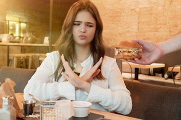 young beautiful woman shows no sign to waiter with fresh meat burger in his hand during lunch in cafe stick to proper nutrition and diet