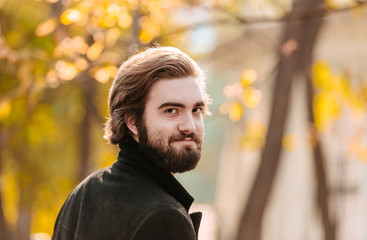 Portrait of young handsome bearded guy, looking back, in the autumn city park.