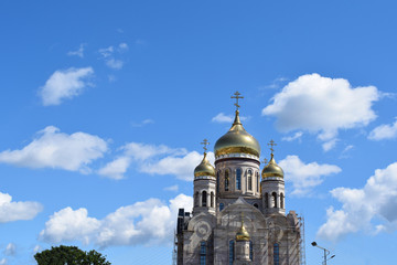 Fototapeta na wymiar Golden domes of an Orthodox church with crosses on background of blue sky with white clouds. Reconstruction of church