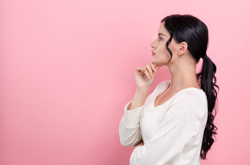 Young woman in a thoughtful pose on a pink background