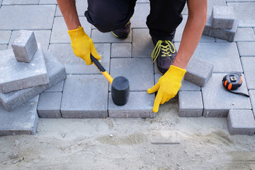 The master in yellow gloves lays paving stones in layers. Garden brick pathway paving by...