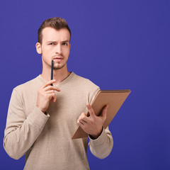 Thinking employee with notebook in left hand holds pen near face in right hand