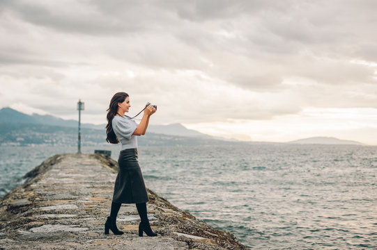 Young beautiful woman taking pictures outside with vintage film camera, wearing black leather skirt