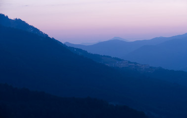 Naklejka premium Evening blue mountains. The sun is setting. In the distant city lights. Sochi, Russia.