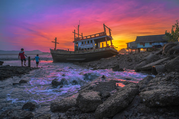 children in fishing village are catching fishes beside the old fishing boat in sunset