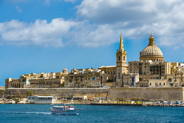 Fototapeta premium A boat on Marsamxett harbour sails pass the city of Valletta, Malta.
