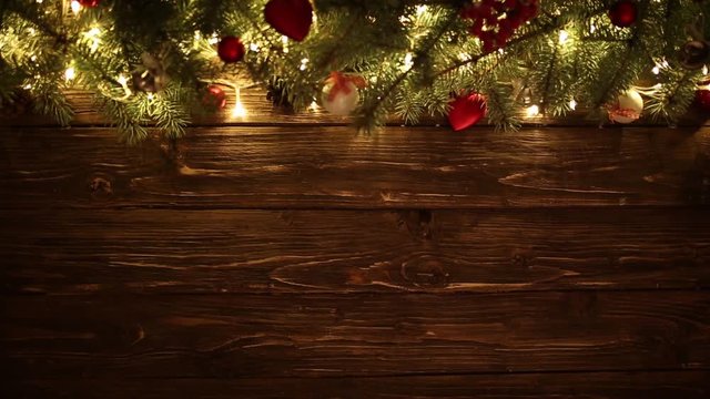 Blurred Christmas background, with fir branches, fairy lights and christmas decorations on brown wooden plank