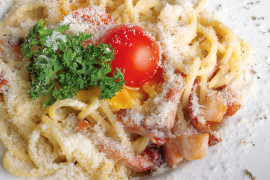 typical spaghetti alla carbonara  with raw egg and bacon. served on a white plate with grated Pecorino cheese. decorated with cherry tomato and parsley. top view close up