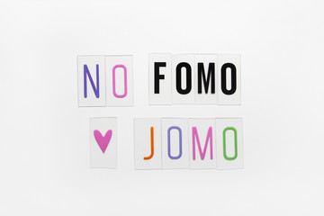 Abbreviation words FOMO, JOMO on transparent plastic on white background. FOMO means Fear Of Missing Out. JOMO - Joy Of Missing Out. Opposition, choice, social problem, digital detox. Flat lay