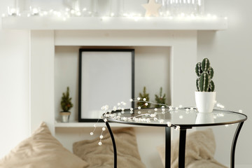 Round glass table with some winter ornaments and decoration with bright white fireplace wall background. Christmas time. Nice luxurious home interior.