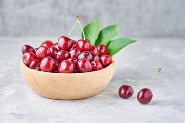 Red fresh cherry beries in wooden bowl on a gray background
