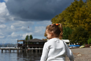 Little girl to lakeshore. In the background a black cloudy sky. Childhood concept. Weather concept.