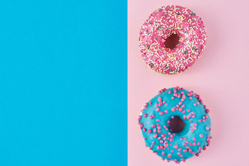 Two donuts glazed with sprinkles on a pink and blue background with copy space, top view flat lay. Minimalism concept