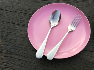 fork and spoon on pink plate with wood background