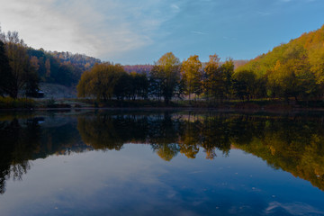 Fototapeta na wymiar Fresh water lake in a former quarry with reflections of the Indian summer and autumn colors of the leaves on an early morning in November