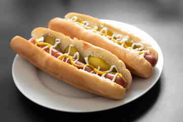 Homemade hot dogs with sausages and pickled cucubers in plate, isolated.