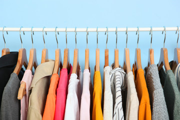 fashionable clothes on hangers on a wardrobe rack on a colored background.