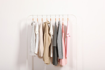 Fashionable clothes on hangers on a wardrobe rack on a light background.