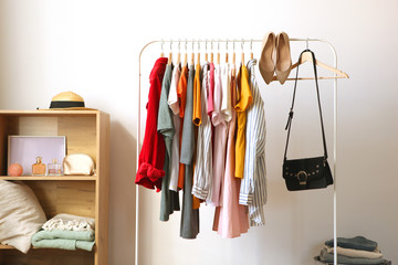 Fashionable clothes on hangers on a wardrobe rack in the background of the room.