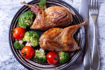 Quail fried whole with broccoli and cherry tomatoes. Black plate, marble background. Selective focus, close up.