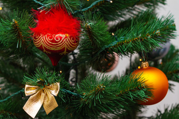 Fototapeta na wymiar A part of christmas tree with red and orange balls, gold bow on faux Christmas tree. New years card, selective focus