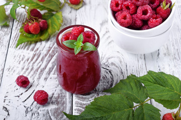 Raspberry jam in the glass jar on the white wooden table