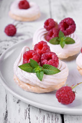Mini Pavlova cakes topped with raspberries and mint on white wooden table
