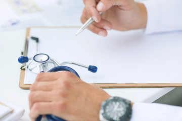Male doctor on duty in white coat reading patient's information with pen in hand, filling prescription or checklist document close-up. Health and medical concept.