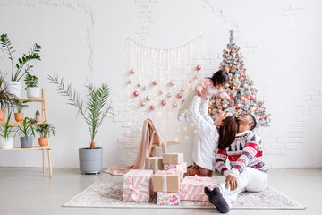 Happy mixed race family african american dad mom and daughter rejoice celebrating Christmas sitting on living room floor in beautiful bright interior with Christmas tree and decorations. Copyspace