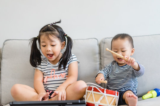 Little sister and her baby brother play with keyboard and drum and singing.Asian child playing and singing happy moment in music time.Sibling child sing in music song class at home.