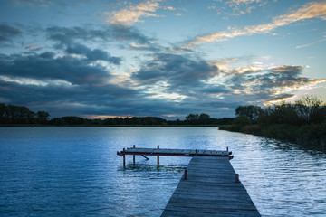 Wooden plank bridge, calm lake and evening clouds on the sky