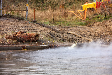A breakthrough in a pipe with hot water, water is pumped out onto the road with a fire truck, pump and fire hose, close-up.