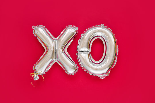 XO foil balloon letters. Love concept. Holiday and celebration. Valentine's Day or wedding/bachelorette party decoration. Silver Metallic air balloons on red background.